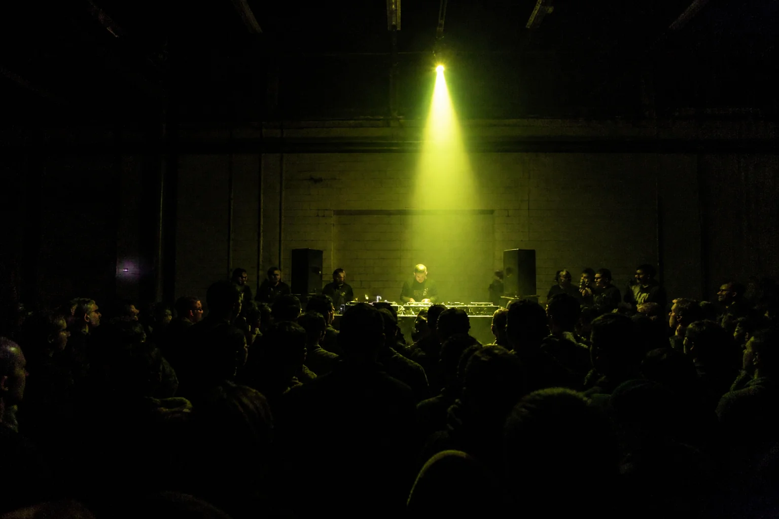 Crowd in a dark warehouse room facing a DJ booth